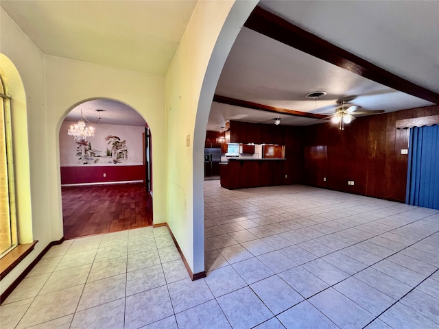 interior space with ceiling fan with notable chandelier, beam ceiling, light tile patterned floors, and wooden walls