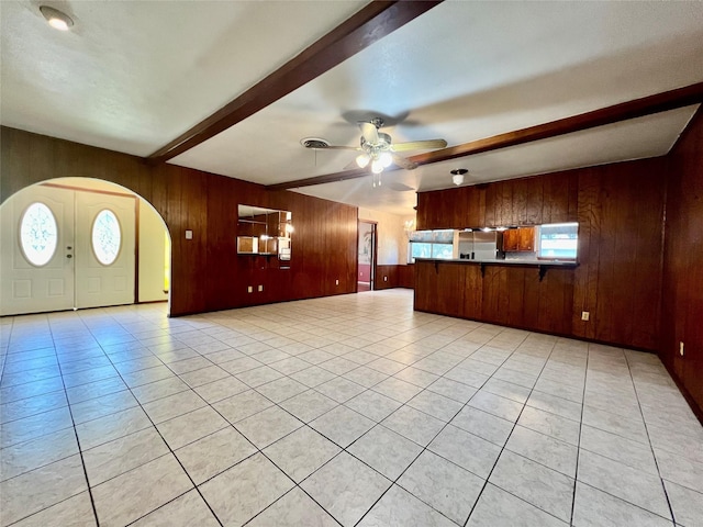 unfurnished living room featuring ceiling fan, light tile patterned floors, wooden walls, and beamed ceiling