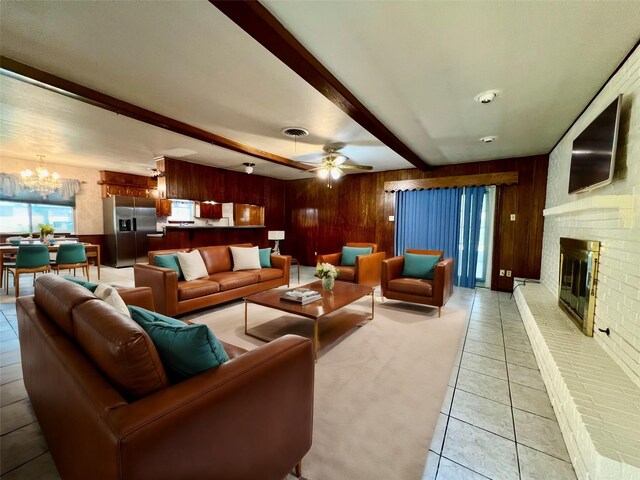 tiled living room with a fireplace, beamed ceiling, ceiling fan with notable chandelier, and wooden walls