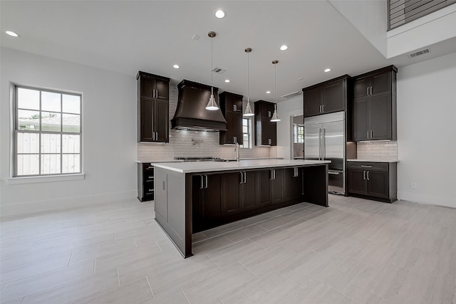 kitchen with pendant lighting, a breakfast bar area, a center island with sink, appliances with stainless steel finishes, and premium range hood