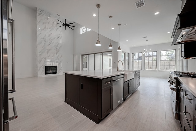 kitchen featuring ceiling fan with notable chandelier, pendant lighting, a high end fireplace, stainless steel appliances, and a kitchen island with sink