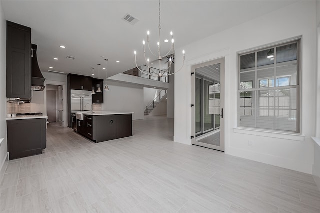 kitchen featuring a kitchen island with sink, tasteful backsplash, hanging light fixtures, custom range hood, and built in fridge