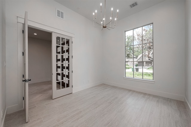 empty room featuring french doors, an inviting chandelier, light wood-type flooring, and a wealth of natural light