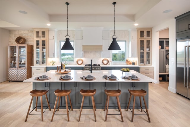 kitchen featuring a center island with sink, backsplash, stainless steel built in refrigerator, and a raised ceiling