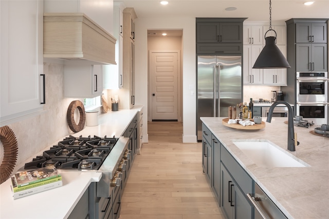 kitchen with light hardwood / wood-style flooring, premium range hood, appliances with stainless steel finishes, decorative light fixtures, and sink