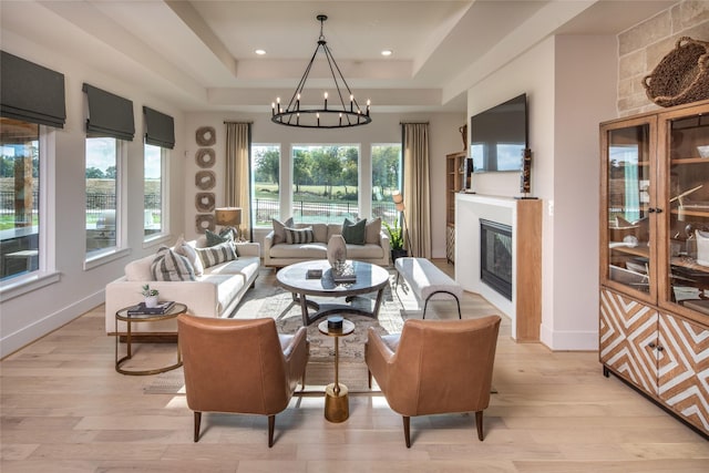 living room with a tray ceiling, light wood-style floors, a chandelier, and a glass covered fireplace
