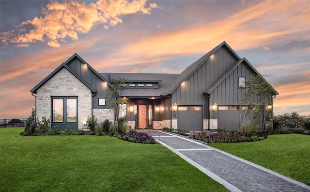 view of front facade featuring board and batten siding, decorative driveway, roof with shingles, a front yard, and stone siding