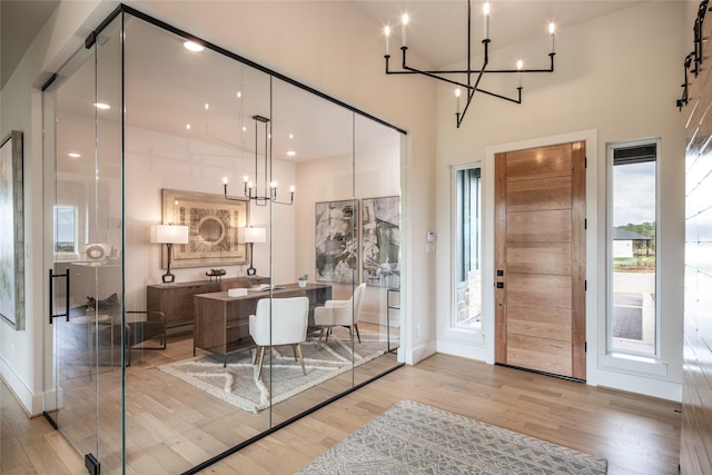 entrance foyer with a high ceiling, a notable chandelier, light wood-style floors, and baseboards