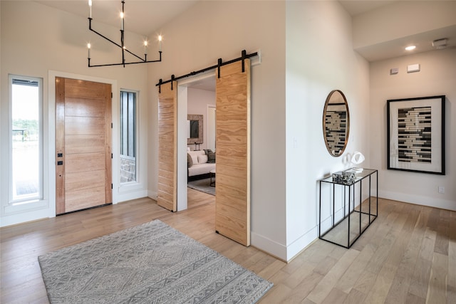 entrance foyer featuring a chandelier, light hardwood / wood-style flooring, a barn door, and a towering ceiling