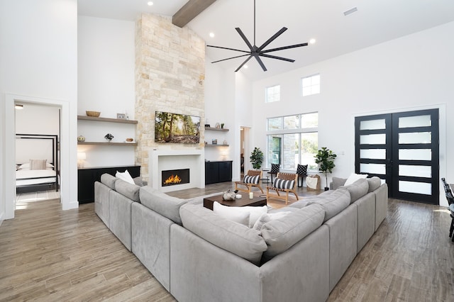 living room featuring beam ceiling, a fireplace, light hardwood / wood-style flooring, and high vaulted ceiling