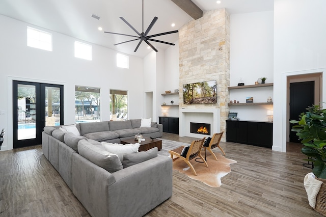 living room featuring ceiling fan, a high ceiling, hardwood / wood-style floors, beamed ceiling, and a stone fireplace