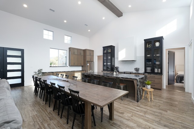 dining area featuring high vaulted ceiling, beamed ceiling, and light hardwood / wood-style flooring