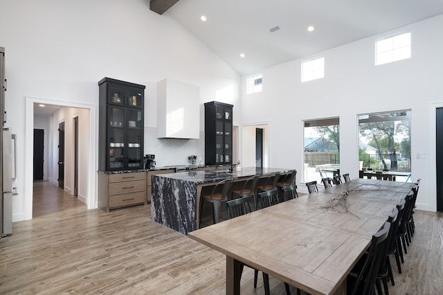 kitchen featuring high vaulted ceiling, light wood-type flooring, dark stone countertops, beam ceiling, and a breakfast bar