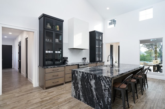 kitchen with a kitchen bar, light hardwood / wood-style flooring, dark stone counters, decorative backsplash, and a large island