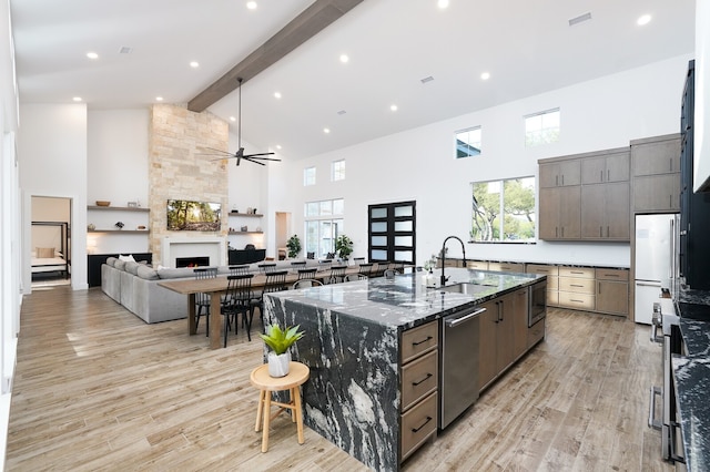 kitchen with light wood-type flooring, dark stone counters, a fireplace, sink, and high vaulted ceiling