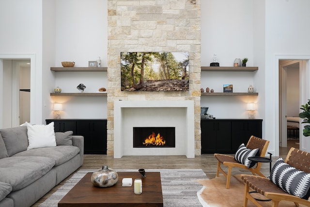 living room featuring a stone fireplace, light hardwood / wood-style flooring, and a high ceiling