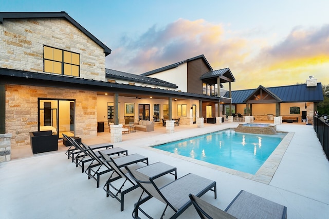 pool at dusk featuring an in ground hot tub and a patio