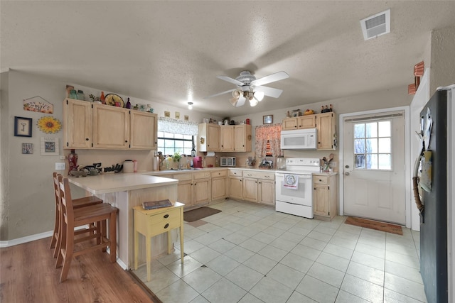 kitchen with sink, a kitchen bar, kitchen peninsula, light brown cabinets, and white appliances