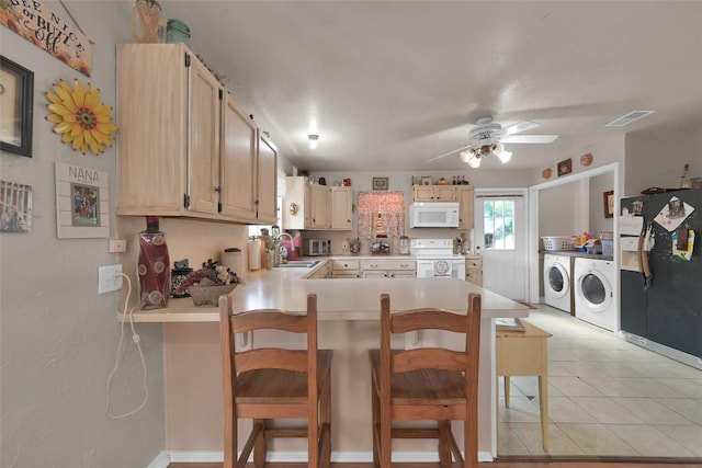 kitchen with white appliances, a breakfast bar, independent washer and dryer, kitchen peninsula, and light brown cabinets