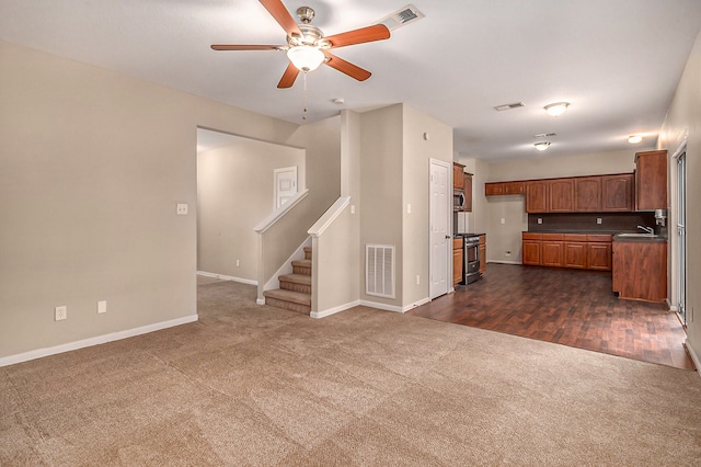 unfurnished living room featuring dark colored carpet, sink, and ceiling fan