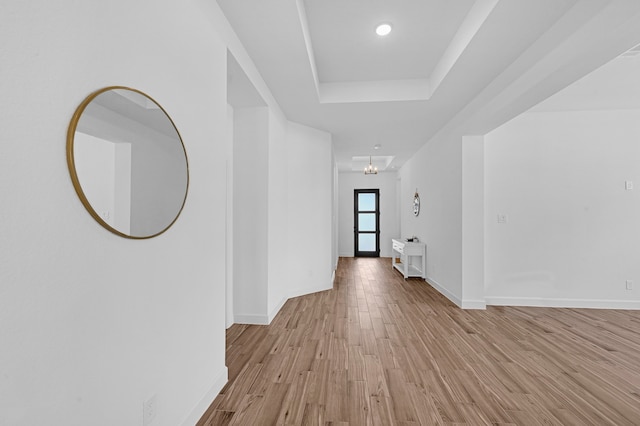 corridor with light hardwood / wood-style floors, a chandelier, and a tray ceiling