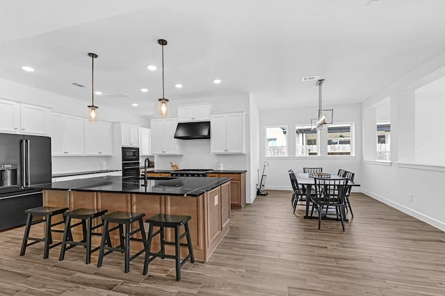 kitchen with sink, black appliances, a large island with sink, pendant lighting, and white cabinets