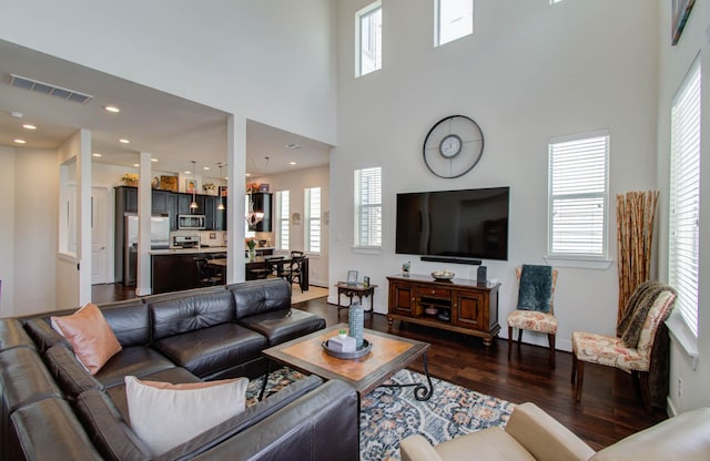 living room featuring a chandelier, plenty of natural light, a towering ceiling, and dark wood-type flooring