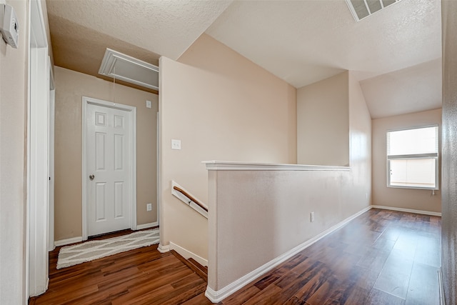 hall featuring dark hardwood / wood-style flooring, a textured ceiling, and vaulted ceiling