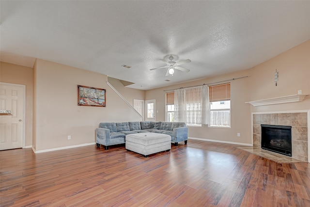 living room featuring hardwood / wood-style flooring, a textured ceiling, a tiled fireplace, and ceiling fan