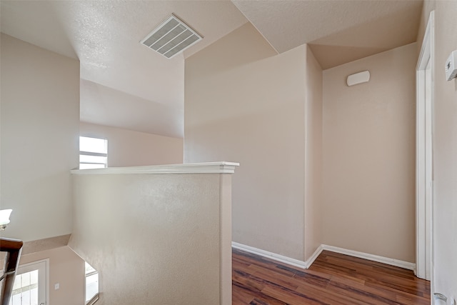 hall featuring a textured ceiling, wood-type flooring, and lofted ceiling