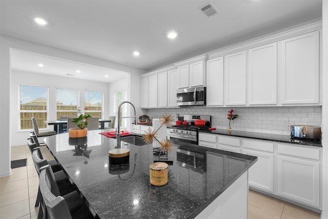 kitchen featuring an island with sink, dark stone counters, sink, white cabinets, and appliances with stainless steel finishes