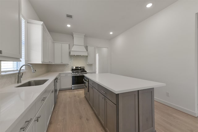 kitchen with premium range hood, sink, white cabinetry, appliances with stainless steel finishes, and a center island