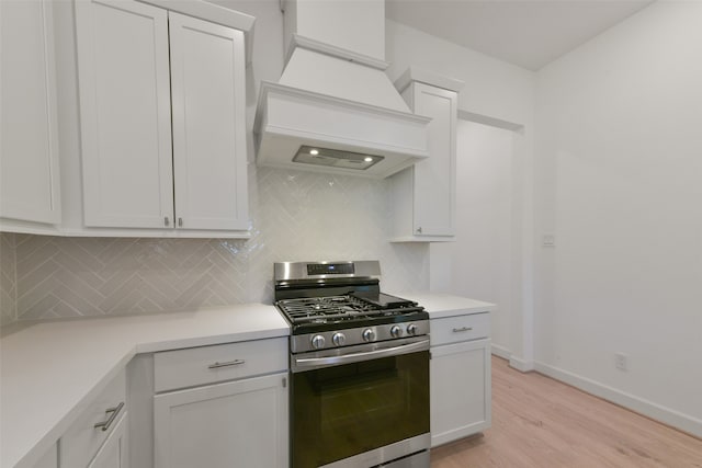 kitchen with light wood-type flooring, white cabinets, custom range hood, backsplash, and gas range