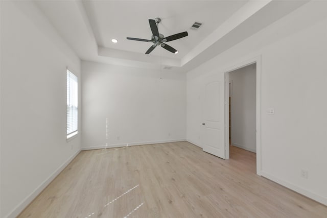 unfurnished room with light hardwood / wood-style flooring, ceiling fan, and a raised ceiling