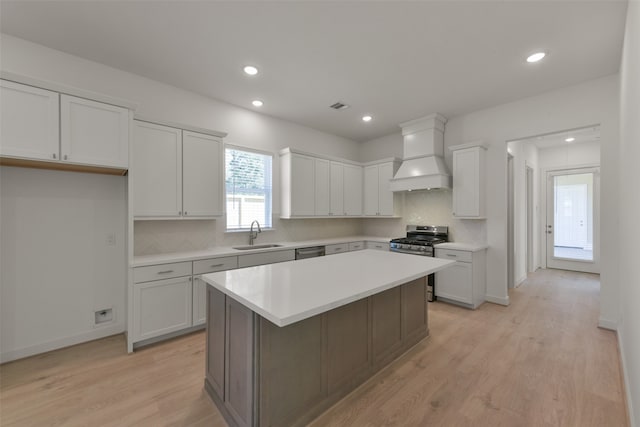 kitchen with custom range hood, white cabinetry, stainless steel appliances, light wood-type flooring, and a center island