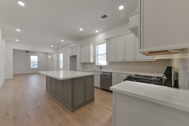 kitchen with light hardwood / wood-style floors, black gas range oven, white cabinets, a center island, and stainless steel dishwasher