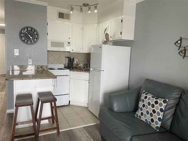 kitchen with white appliances, white cabinets, track lighting, hardwood / wood-style floors, and decorative backsplash