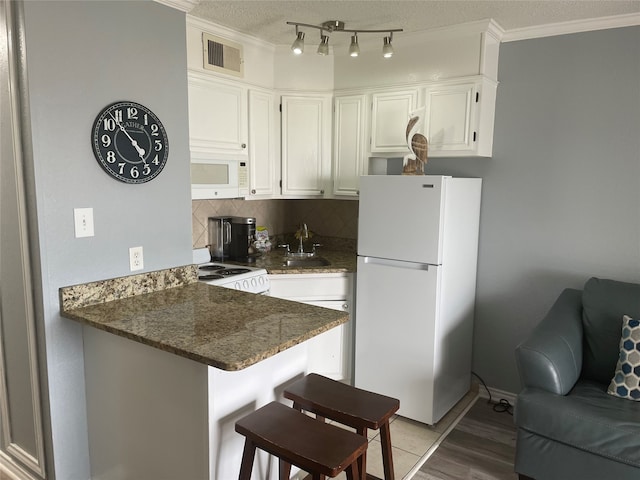 kitchen featuring tasteful backsplash, white appliances, dark stone counters, kitchen peninsula, and white cabinetry