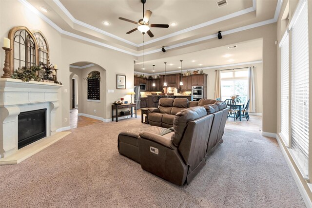 living room featuring crown molding, light carpet, a raised ceiling, ceiling fan, and a fireplace