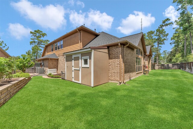 rear view of house with a yard, central AC unit, and a storage unit