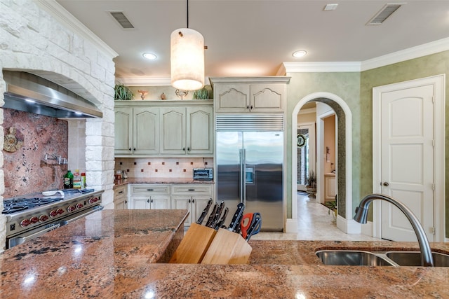 kitchen featuring tasteful backsplash, high end appliances, crown molding, sink, and decorative light fixtures