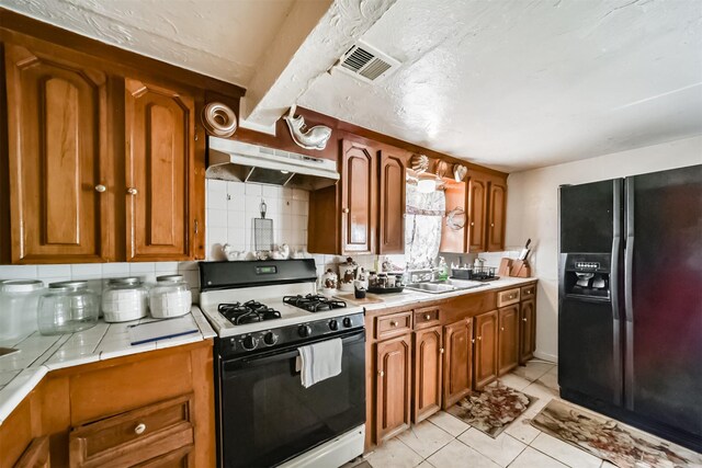 kitchen featuring black fridge, white range with gas cooktop, tile counters, light tile patterned floors, and backsplash