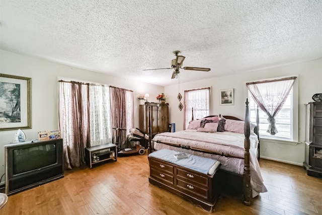 bedroom featuring a textured ceiling, light hardwood / wood-style flooring, multiple windows, and ceiling fan