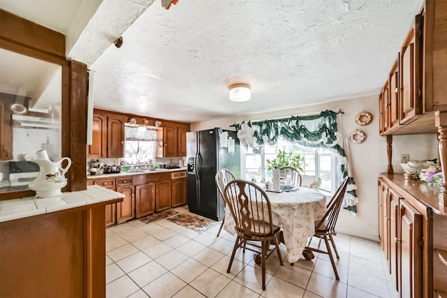 kitchen with plenty of natural light, black fridge with ice dispenser, tile counters, and light tile patterned floors