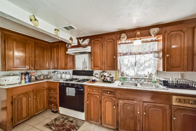 kitchen featuring light tile patterned flooring, tile counters, backsplash, white range with gas stovetop, and sink