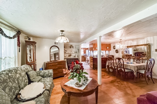 living room featuring a notable chandelier, a textured ceiling, built in features, and hardwood / wood-style floors