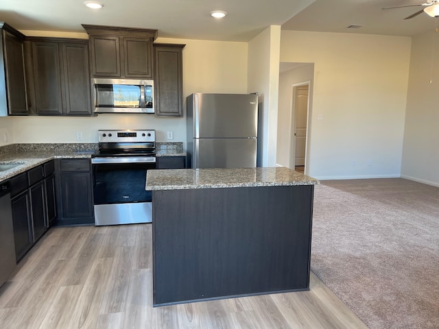 kitchen with a center island, light wood-type flooring, appliances with stainless steel finishes, light stone countertops, and ceiling fan