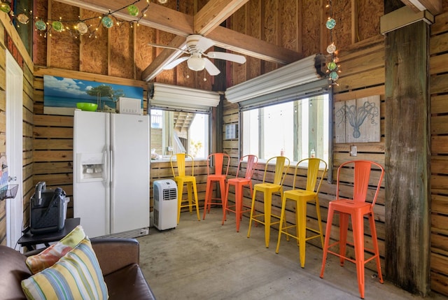 interior space with wood walls, white refrigerator with ice dispenser, and ceiling fan