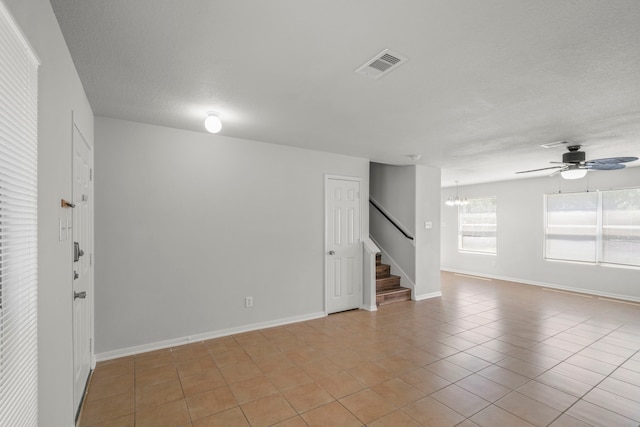 empty room featuring ceiling fan with notable chandelier and light tile patterned floors