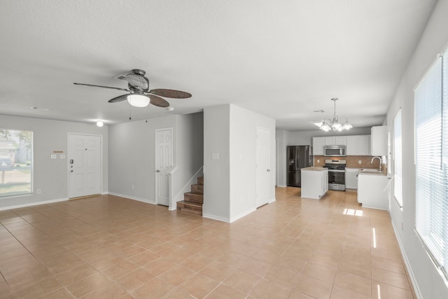 unfurnished living room featuring ceiling fan with notable chandelier, a healthy amount of sunlight, sink, and light tile patterned floors